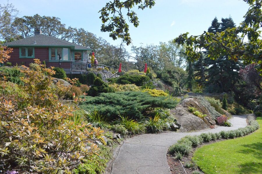 Scenic pathway leads through Abkhazi Garden to a charming house surrounded by lush greenery in Victoria, Canada.