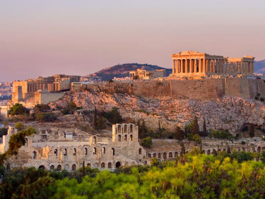Acropolis of Athens at sunset, featuring the Parthenon and Odeon of Herodes Atticus ruins.