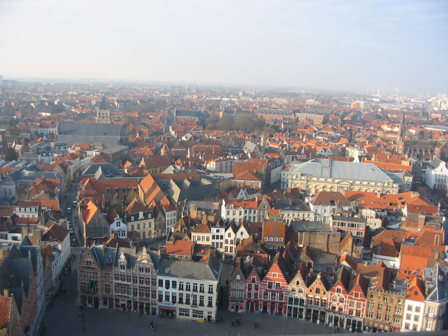 Aerial view of Bruges, showcasing the city's historic architecture and canals against a clear blue sky.