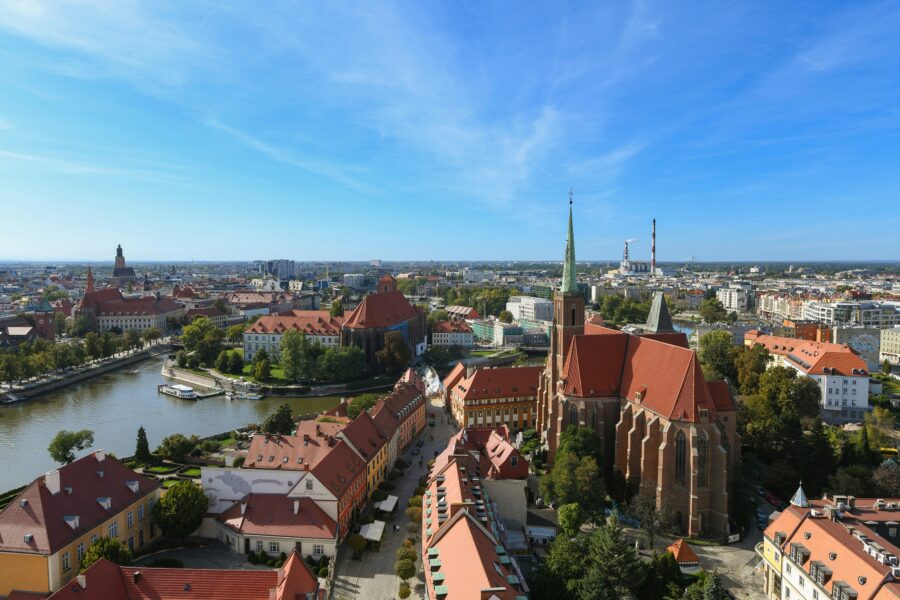 Aerial view of historic European river city with red-tiled roofs and large Gothic brick church.