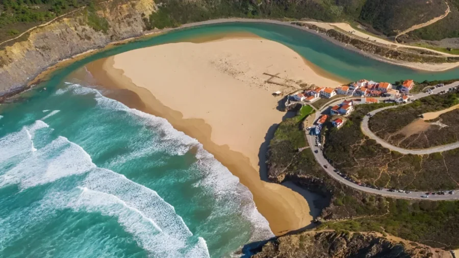 Aerial view of Odeceixe crescent beach and lagoon with red-roof houses, Portugal.