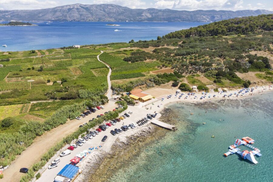 Aerial coastal beach with turquoise water, inflatable water park, pier, and seaside cafe.
