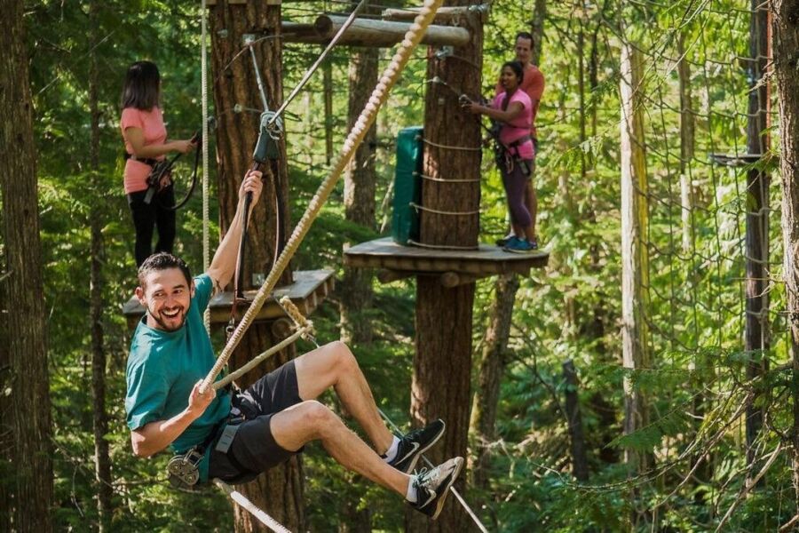 Man traverses a rope course in the woods at Cougar Mountain, showcasing an aerial obstacle challenge.