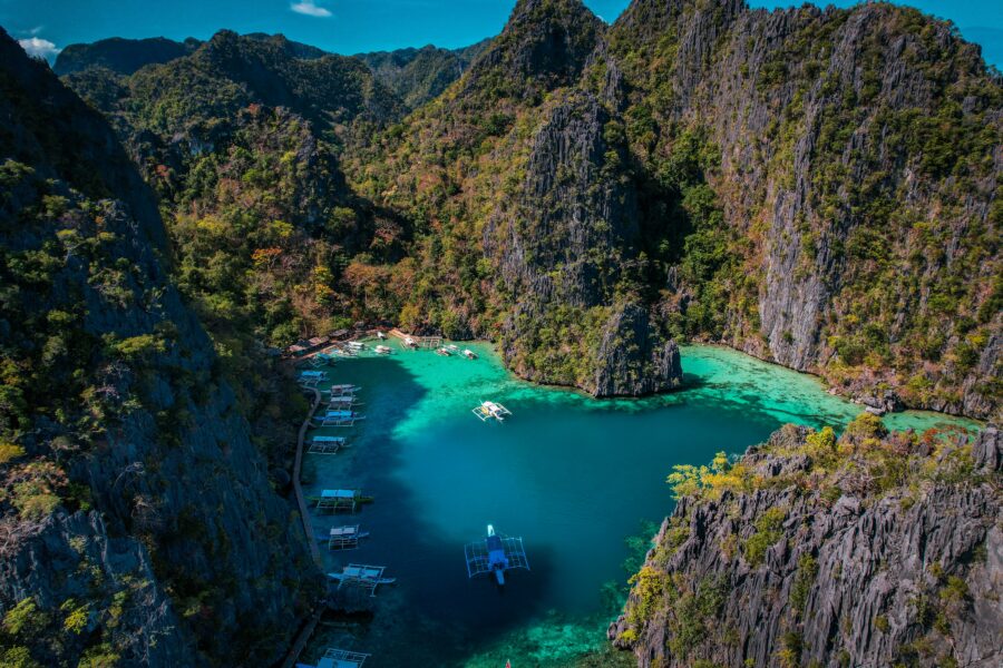 Aerial view of hidden tropical turquoise lagoon surrounded by towering limestone cliffs and moored boats.