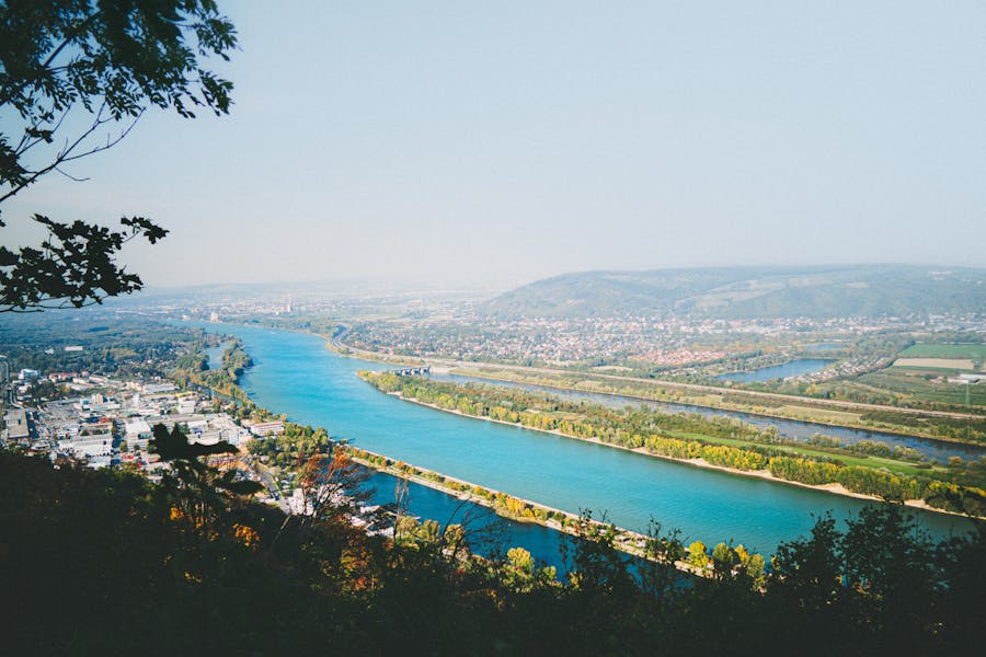 Aerial panorama of the turquoise Danube River valley and Vienna riverbanks.