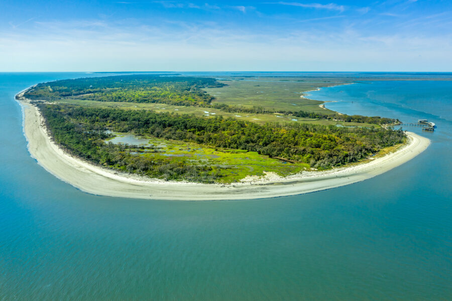 Aerial view of Jekyll Island showcasing lush greenery, sandy beaches, and winding coastal roads under a clear blue sky.