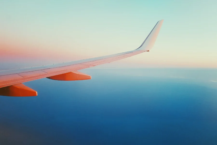 Airplane wing sunset view: serene sky, ocean horizon, twilight hues, adventure travel.