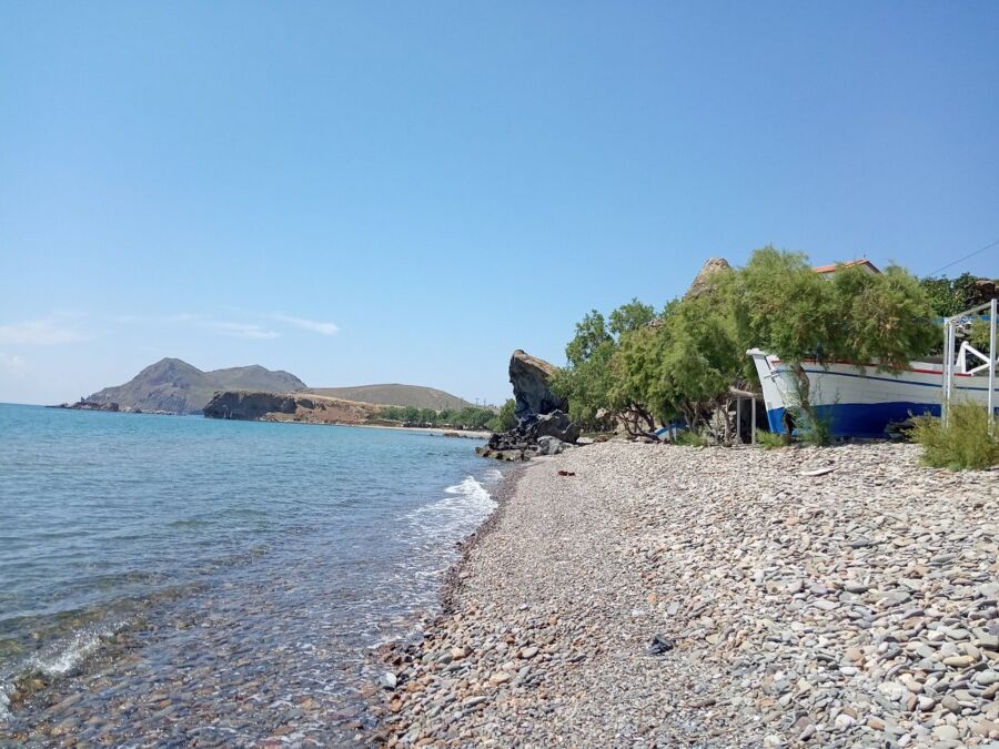 Scenic view of Agios Ioannis beach in Mykonos, showcasing a boat and a charming blue and white house.
