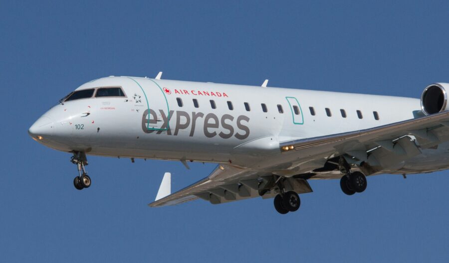 Air Canada Express plane landing, clear sky, extended landing gear, showcasing branding.