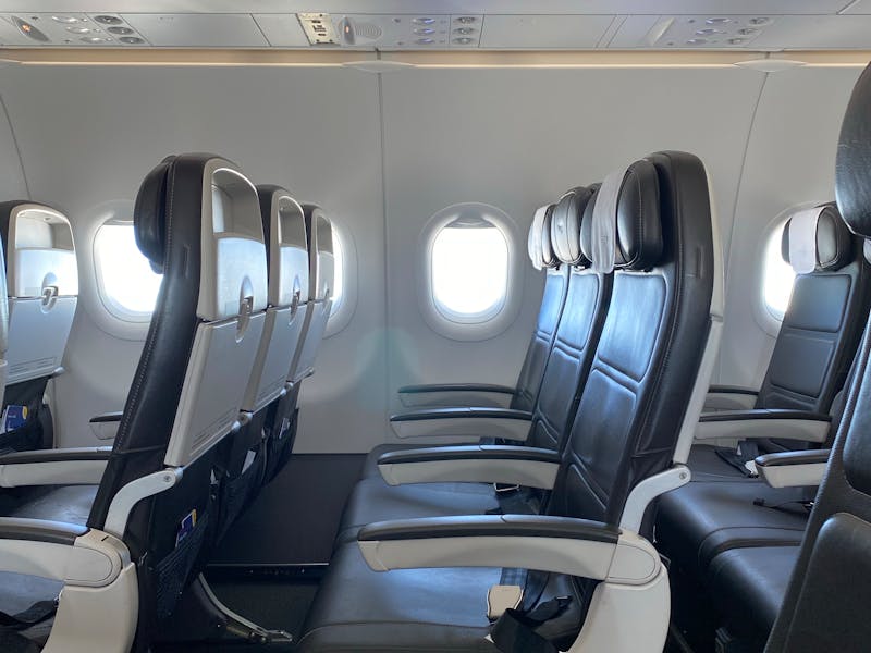 Modern airplane cabin with black leather seats, adjustable armrests, and round windows.