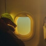 Passenger sleeping in a cozy, serene airplane cabin at sunrise, wearing a green cap.