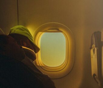 Passenger sleeping in a cozy, serene airplane cabin at sunrise, wearing a green cap.
