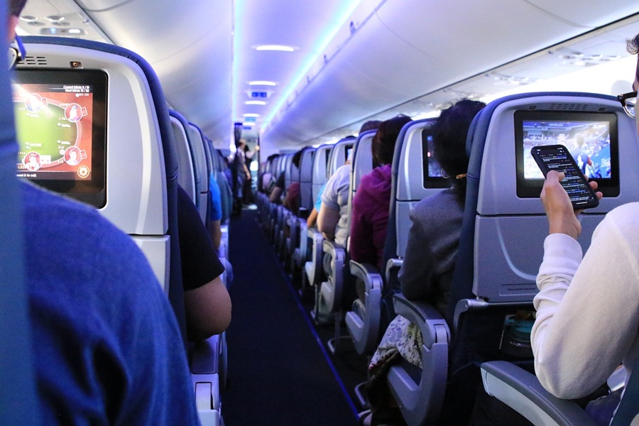 Modern airplane cabin with passengers using in-flight entertainment and personal devices.