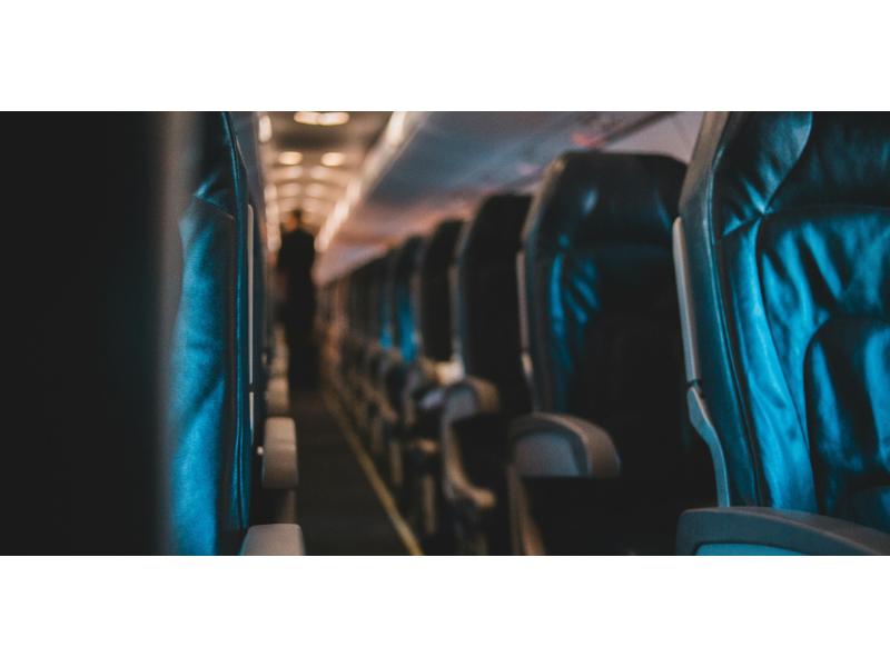 Airplane cabin with leather seats, aisle view, dim lighting, and flight attendant silhouette.
