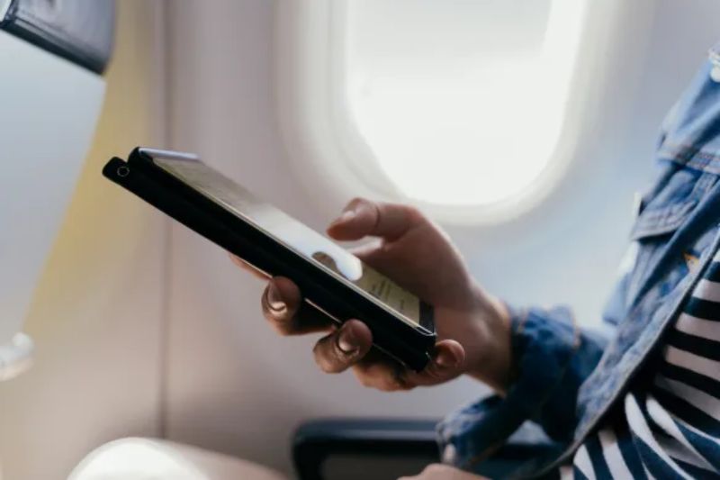 Traveler reading on tablet in airplane, natural light from window, casual attire.