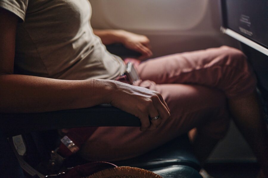 Passenger relaxing by airplane window with stylish attire and silver ring.