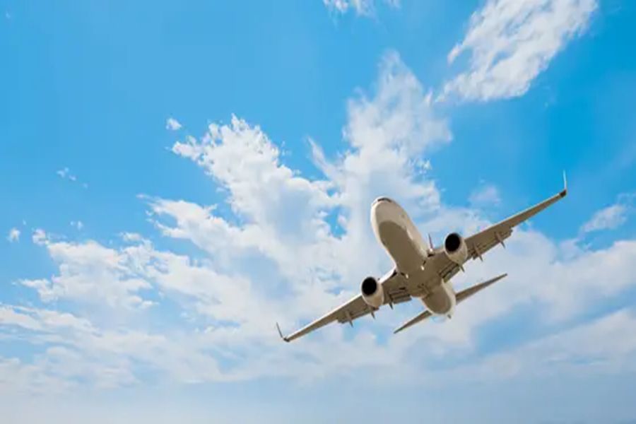 Twin-engine commercial airliner climbing, underbelly and turbofan engines visible against blue sky.