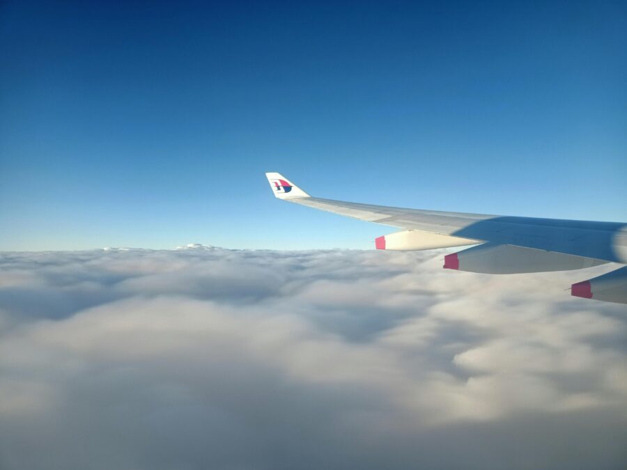 Aerial view of a Malaysian Airlines wing above clouds with clear blue sky.