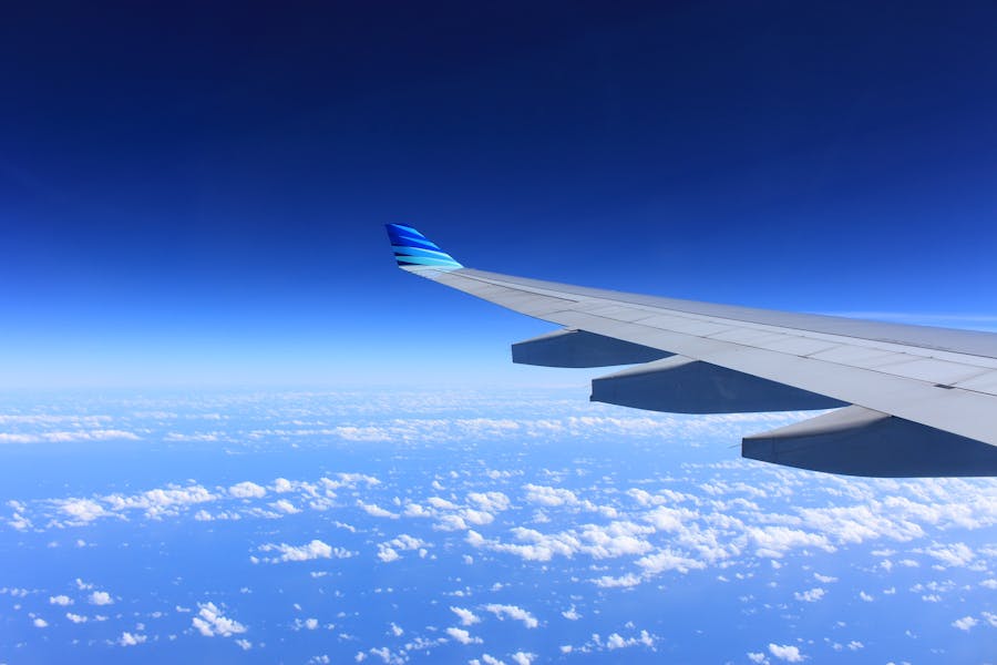 Airplane wing and winglet over fluffy clouds and deep blue sky, aerial flight view.