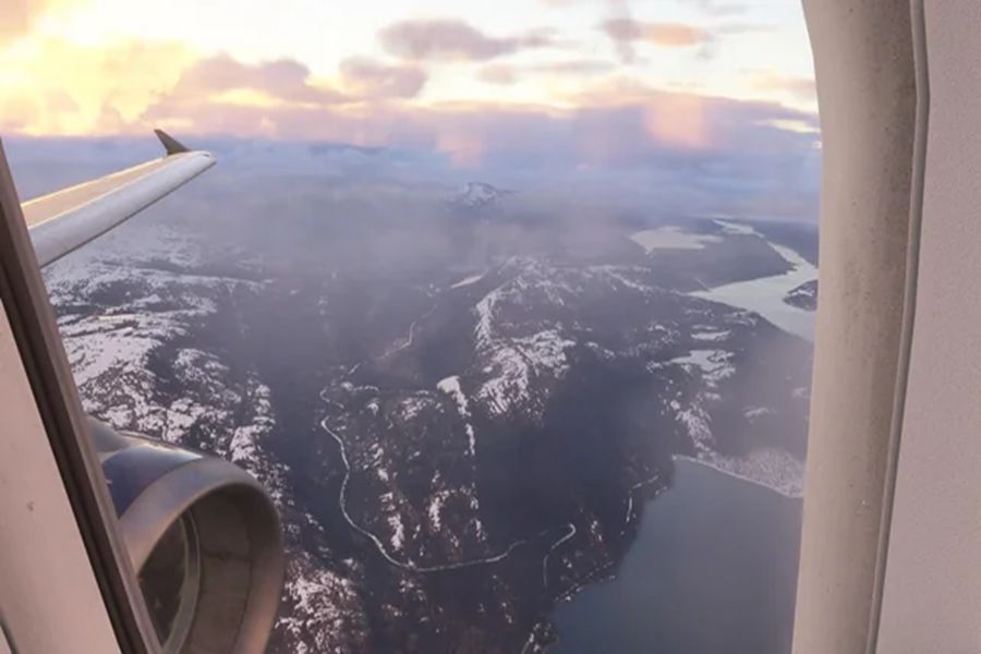Airplane window view over Bodø mountains, coastal fjords, and sunset-lit wing.