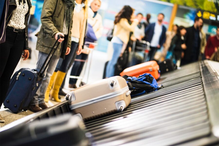 Travelers await luggage at busy airport carousel, showcasing diverse styles and dynamic atmosphere.