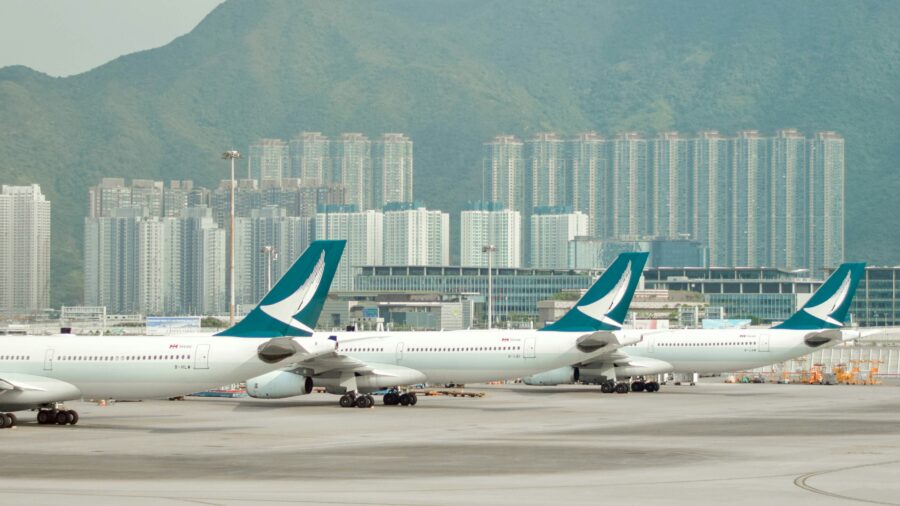 Bustling airport scene with Cathay Pacific planes, urban skyline, and mountain backdrop.