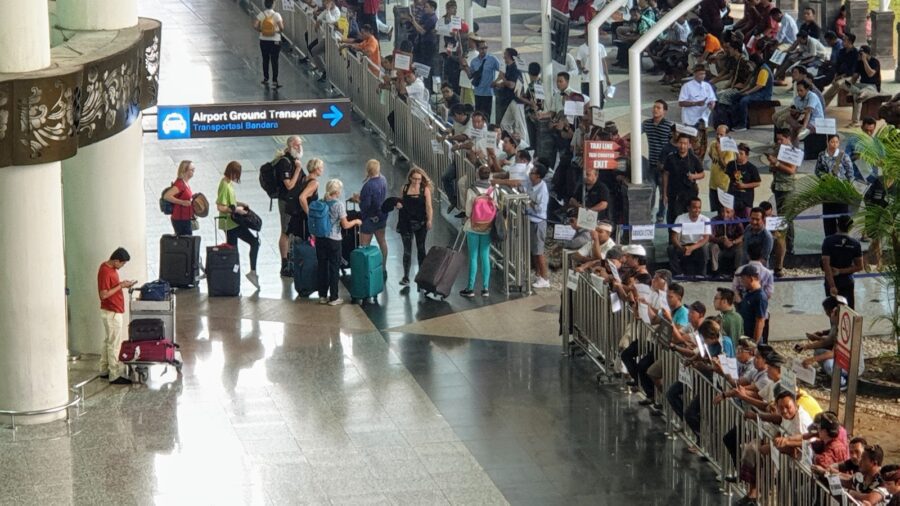 Busy airport terminal with travelers, luggage, and signs for ground transport.