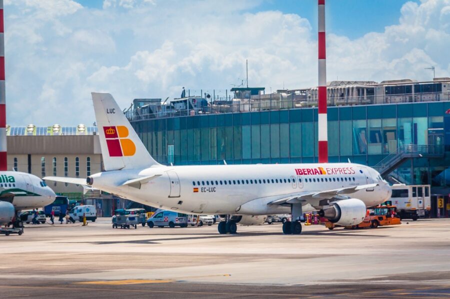 Bustling airport with Iberia Express and Italian airline planes on a sunny day.