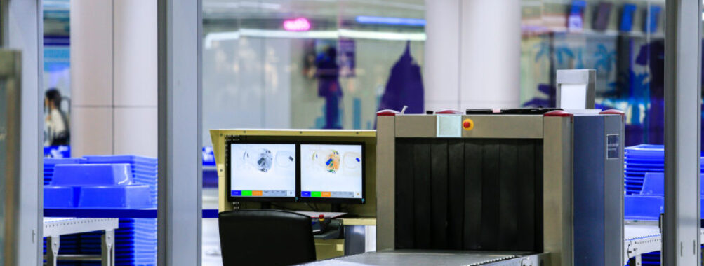 Security checkpoint at an airport with a metal detector and X-ray scanner for passenger and baggage screening.