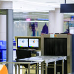 Security checkpoint at an airport with a metal detector and X-ray scanner for passenger and baggage screening.