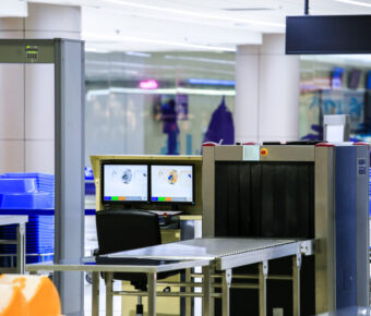 Security checkpoint at an airport with a metal detector and X-ray scanner for passenger and baggage screening.
