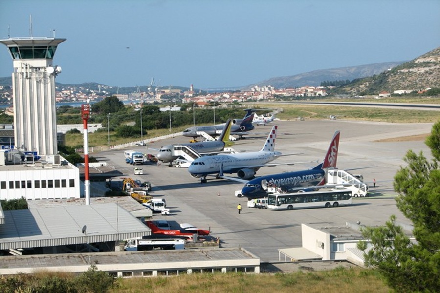 Bustling Split airport tarmac scene with airplanes, control tower, and support vehicles.