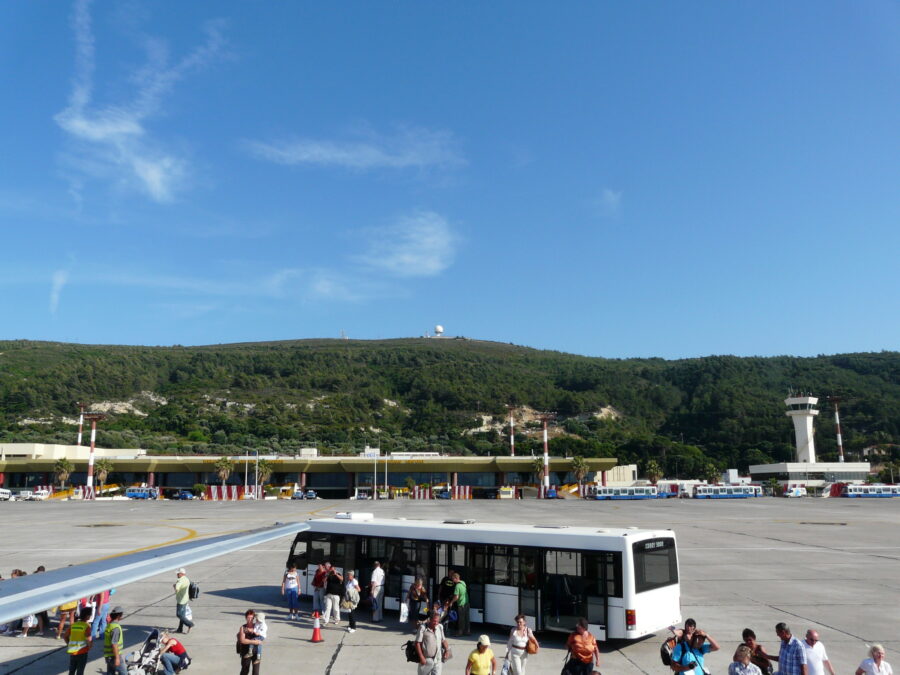 Rhodes airport tarmac with passengers, transfer bus, terminal and control tower.