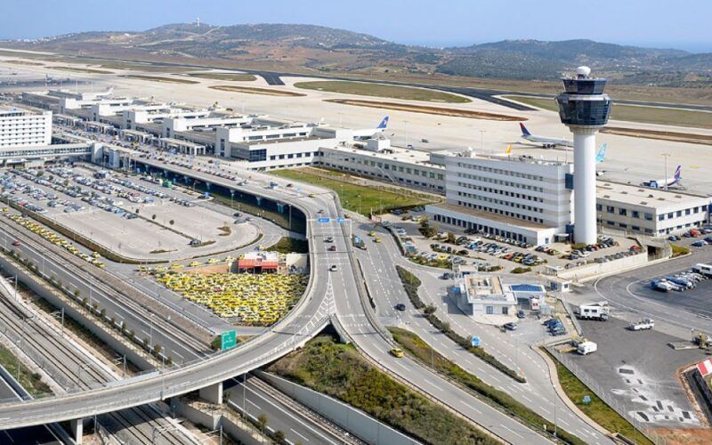 Athens International Airport aerial view: terminal, control tower, runways, taxis, and road ramps.