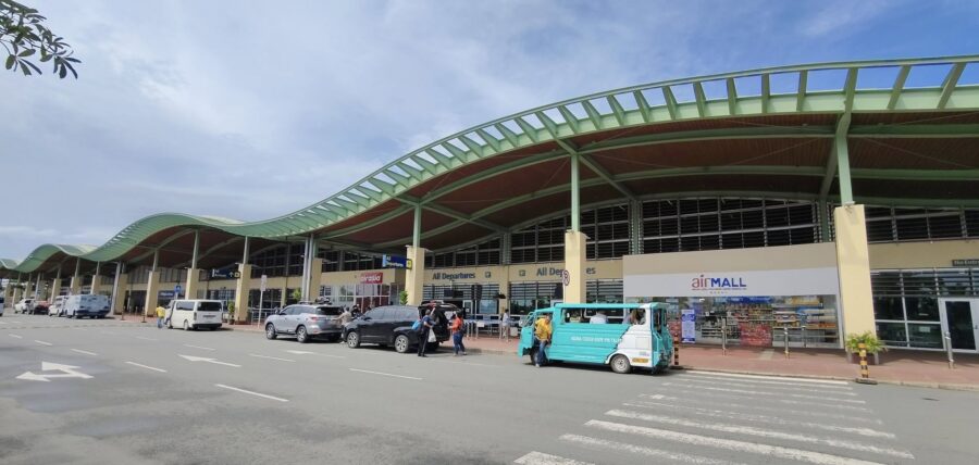 Panglao International Airport curbside terminal with green wave roof, arrivals vehicles and passengers.