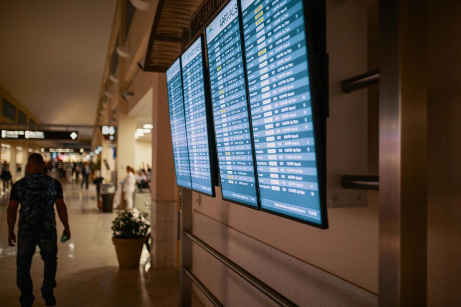 Busy airport corridor with travelers, flight information screens, and signage guiding passengers.