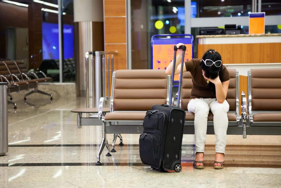 Distressed traveler waiting at modern airport terminal with suitcase, experiencing travel fatigue.