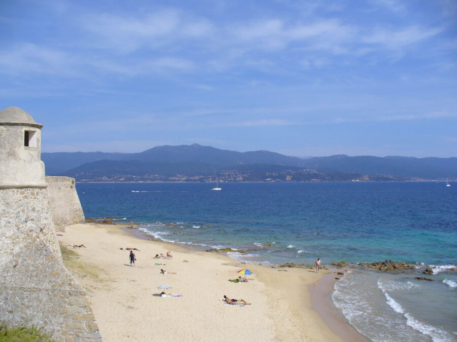 Sandy beach in Ajaccio, Corsica, France, with gentle waves lapping at the shore under a clear blue sky.
