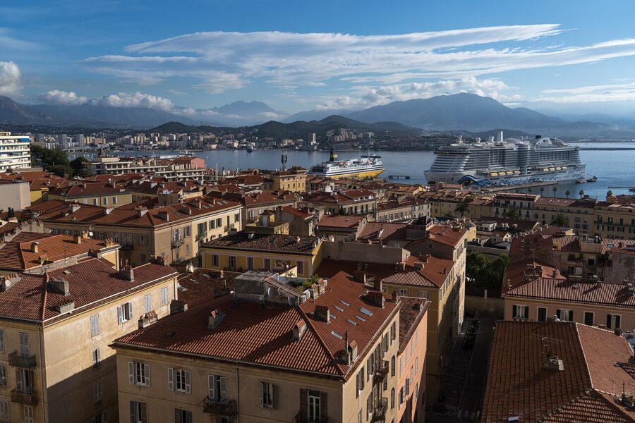Large cruise ship sails in the distance, set against the panoramic view of Ajaccio, Corsica, France.