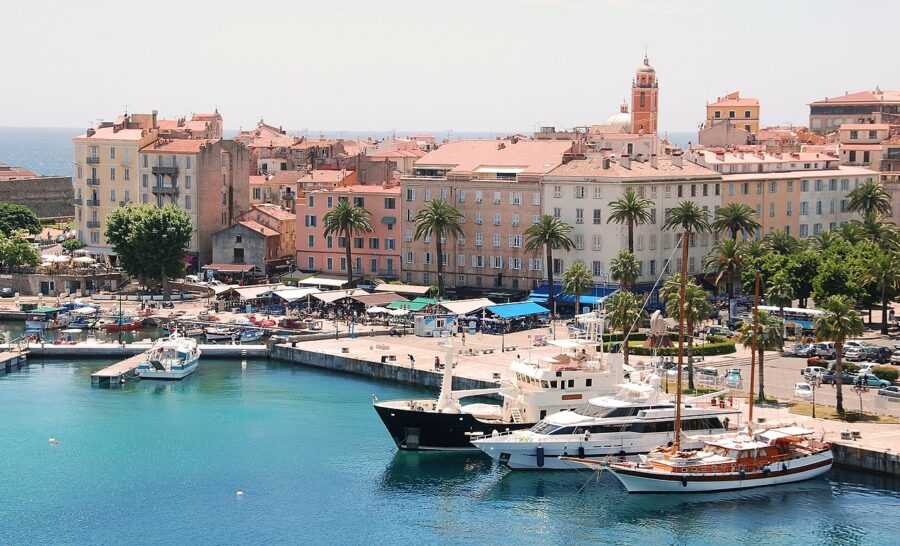 Coastal skyline of Ajaccio, Corsica, featuring colorful buildings and the Mediterranean Sea under a clear blue sky.