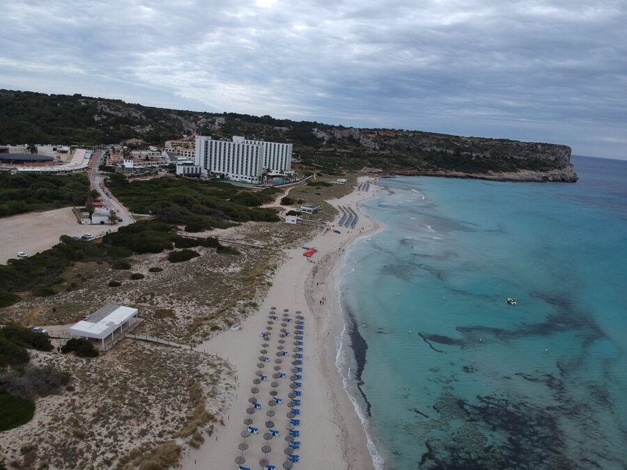Scenic beach in Alaior Menorca with vibrant umbrellas and beach chairs arranged on the shoreline.