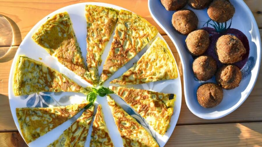 Plate with omelet slices arranged in a circular pattern alongside a dish of round meatballs on a wooden table, conveying a casual and inviting meal setting at the Alghero Wine Tasting