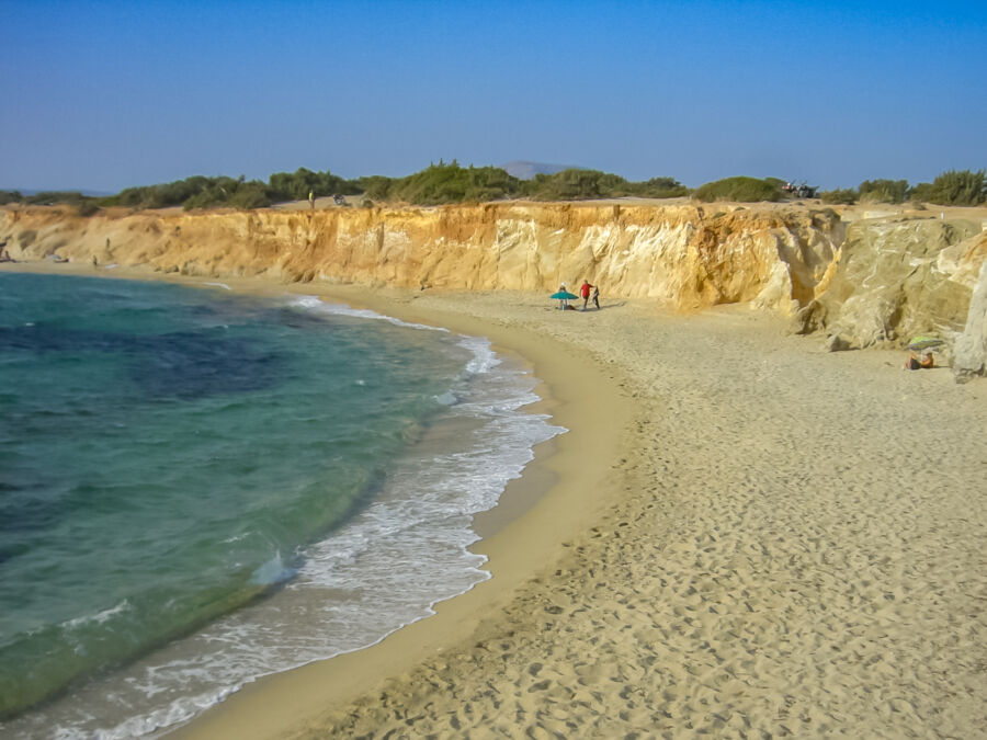 Aliko Beach in Naxos, Greece, showcasing golden sand and a dramatic cliff rising from the shoreline.