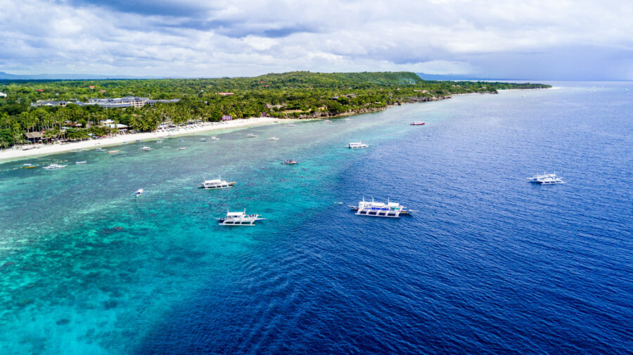Aerial view of Alona Beach in Panglao, Bohol, showcasing its white sand and clear blue waters under a sunny sky.