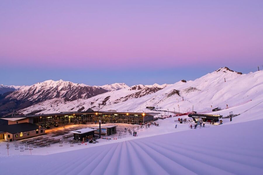 Alpine ski resort at dawn in Queenstown with snowy mountains, ski lifts, and groomed slopes.