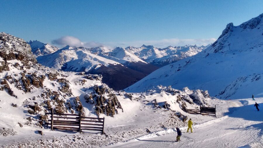 Skiers on sunny alpine ski slope with snowy mountain peaks and blue sky in Patagonia.