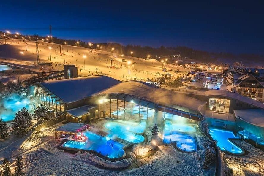 Night view of Zakopane ski resort with snow, steaming thermal baths, and illuminated pools.