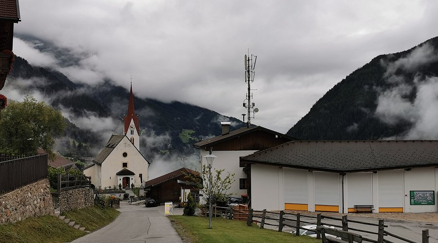 Alpine village church with red steeple in misty mountain valley.