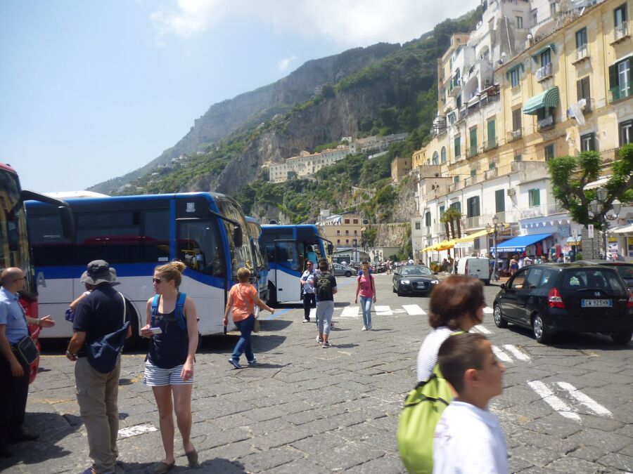 Group of people walking along a street near the Amalfi Coast Blue Bus, surrounded by scenic coastal views.
