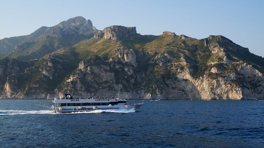 Amalfi Coast ferry sailing through the ocean, surrounded by mountains under a bright sky.